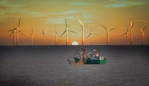 Offshore wind turbines on the horizon with a fishing trawler in the foreground